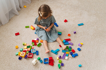 Naklejka premium A little girl playing with colorful rainbow colored constructor pieces on floor in children room. Educational games for Colors sorting. Developing Montessori toddlers activities.