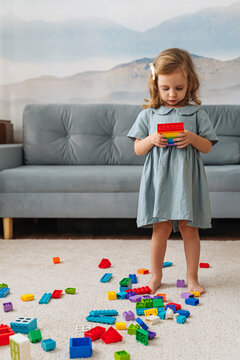 Child builds a tower from rainbow colored constructor pieces. A little girl playing with colorful stackable plastic toy bricks in playroom. Educational game for toddler in modern children room.
