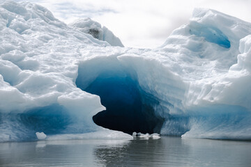 View of a blue iceberg broken off from the glacier tongue of Fjallsjökull in the glacier lagoon Fjallsárlón in Iceland on a cloudy day. With a view of Öræfajökull in the background.