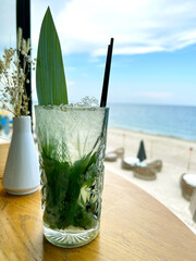 Refreshing mojito in a glass on a table with sea background. Summer cool drink. Mint, lime and...