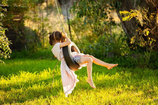 Young country kid in dress swinging on tyre swing in tree outside