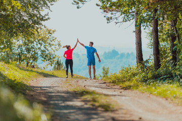 Obraz premium Couple enjoying in a healthy lifestyle while jogging on a country road through the beautiful sunny forest, exercise and fitness concept
