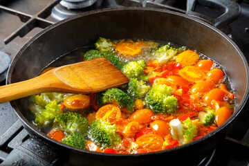 Stewed vegetables bright beans broccoli tomatoes stewed with spices in a frying pan with a spatula.