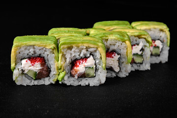 Tuna roll with avocado on top on black concrete