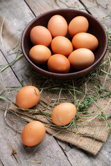 Brown chicken eggs in a bowl on a background of hay and wooden boards.