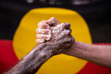 Reconciliation concept - indigenous hand clasped in front of aboriginal flag