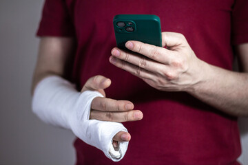 A man in a red T-shirt with a broken arm in a cast holds and uses a phone Close-up