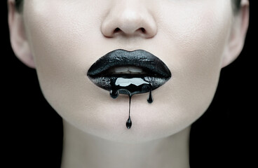 Black Paint dripping from the black lips, dark liquid drops on beautiful model girl's mouth. Lipstick. Halloween party make-up, gothic style. Beauty woman face makeup close up.