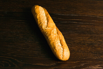 Appetizing french baguette with crust on dark wooden table, background with space for text