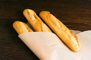 Delicious baguettes from the bakery wrapped in baking paper, on a dark wooden background