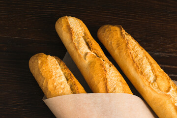 Delicious baguettes from the bakery wrapped in baking paper, on a dark wooden background