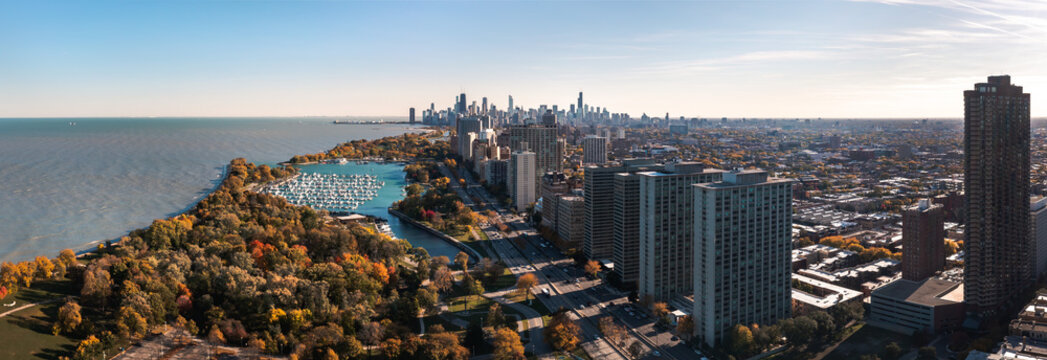 Beautiful cityscape aerial panorama of the Lakeview neighborhood lakefront with autumn foliage surrounding Belmont Harbor and the Chicago skyline in the distance on a sunny day.