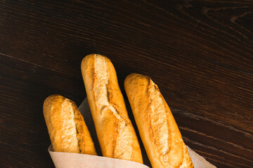 Delicious baguettes from the bakery close-up, wrapped in baking paper, on a dark wooden background with copy space