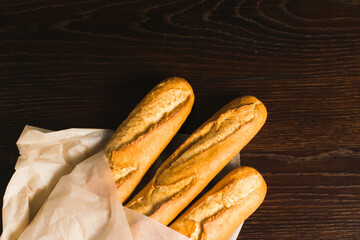 Delicious baguettes from the bakery wrapped in baking paper, on a dark wooden background