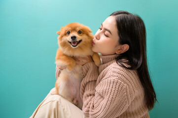 Portrait of Young beautiful woman kisses and hugs her dog over green background.