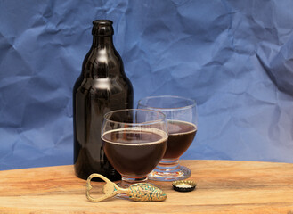 Still life with dark brown craft beer bottle on a wooden board against dark blue background