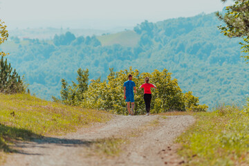 Obraz premium Couple enjoying in a healthy lifestyle while jogging on a country road through the beautiful sunny forest, exercise and fitness concept
