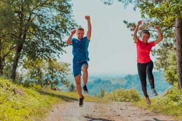 Obraz premium Couple enjoying in a healthy lifestyle while jogging on a country road through the beautiful sunny forest, exercise and fitness concept