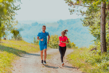 Fototapeta premium Couple enjoying in a healthy lifestyle while jogging on a country road through the beautiful sunny forest, exercise and fitness concept