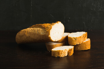 Fototapeta premium French baguette with appetizing crust cut into pieces on wooden table close-up, dark wooden background with copy space