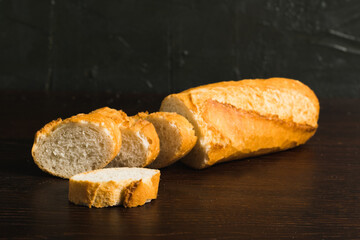 Fragrant fresh French baguette with crust on dark wooden background, side view
