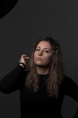 a woman with curly hair on a dark background, a woman over 30 years old showing negative emotions, a portrait of a tense face in dark clothes