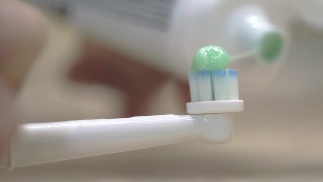 Macro shot of a man's hand pouring toothpaste into an electric toothbrush.