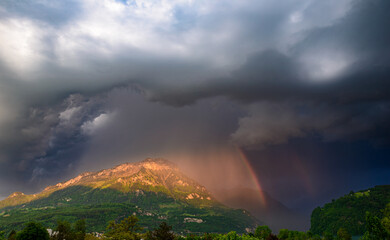 Storm front over the Alps mountains in Switzerland. Rain clouds and rainbow. - 561306349