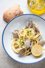 Plate of spaghetti with littleneck clams, lemon zest and chopped parsley, vertical shot on a beige stone background, middle closeup