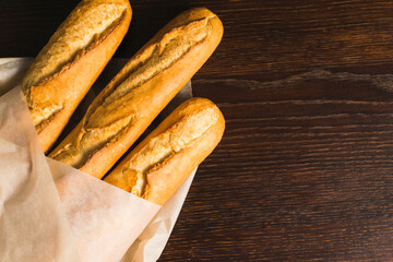 Delicious baguettes from the bakery close-up, wrapped in baking paper, on a dark wooden background...