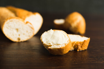 A slice of baguette with butter macro on a wooden background. Sliced French baguette on a dark wooden table