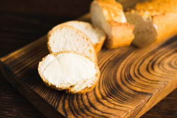 A slice of baguette with butter macro on a wooden background. Sliced French baguette on a wooden cutting board