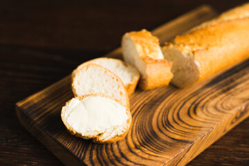 A slice of baguette with butter macro on a wooden background. Sliced French baguette on a wooden cutting board