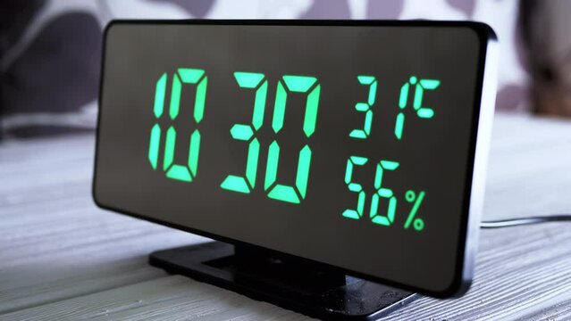 Digital Clock Showing Time on Green Display 10:30 AM, Temperature, Air Humidity. Modern mirror clock, alarm clock with a thermometer, hydrometer standing on a desk on white background. Time concept.