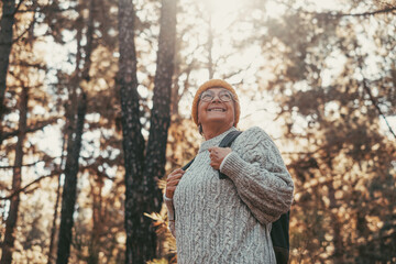 Head shot portrait close up of middle age caucasian woman walking and enjoying nature in the middle of trees in forest. Old mature female wearing glasses trekking and discovering. - Powered by Adobe