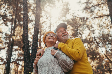 Head shot portrait close up of middle age cheerful people smiling and looking at the the trees of the forest around them. Active couple of old seniors hiking and walking together in the mountain 