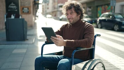 Young hispanic man using touchpad sitting on wheelchair at street