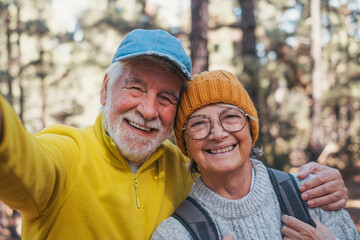 Head shot portrait close up of cute couple of old seniors taking a selfie together in the mountain forest looking at the camera smiling having fun enjoying. Two mature people hiking.