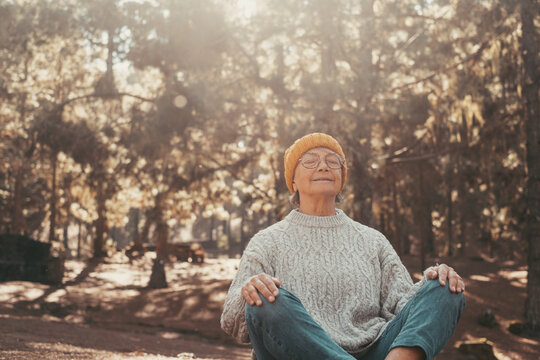 Head shot portrait close up of one middle age old woman resting and relaxing doing yoga in the forest of mountain in the nature. One mature female person enjoying having fun lifestyle..