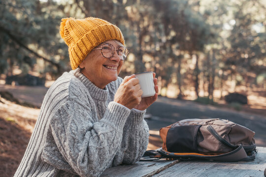 Head shot portrait close up of middle age woman relaxing drinking coffee or tea sitting at table in the forest of mountain in the middle of nature. Autumn season enjoying concept lifestyle.