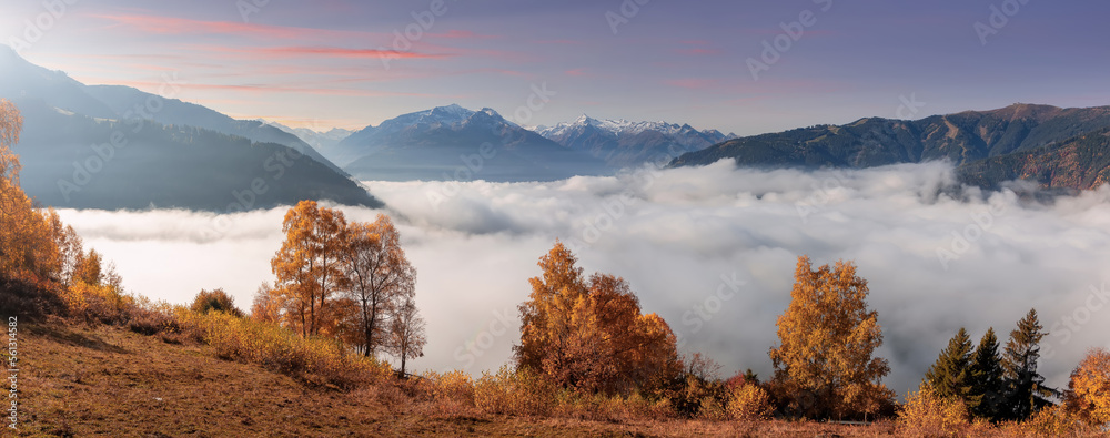 Fototapete Colorful foggy morning in the Alps mountains. autumn foggy scenery. Amazing nature background. Mountainous autumn landscape. Red folliage on trees and fog in the distant valley. Zell am see lake