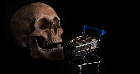 Human skull and coins of different countries in a miniature shopping cart on a black background