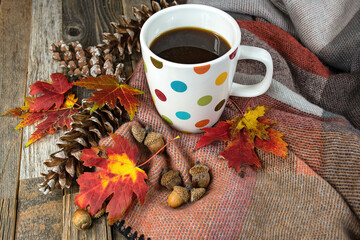 Polka dot coffee mug on a soft blanket with autumn leaves, acorns, and pine cones
