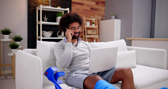 Happy Young Man With Broken Leg Sitting On Sofa Talking