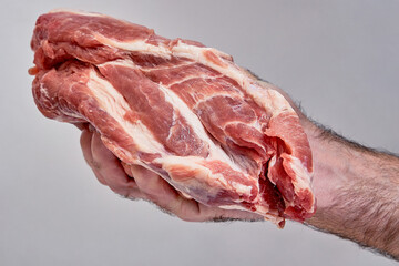 a man's hand holds a piece of raw meat.