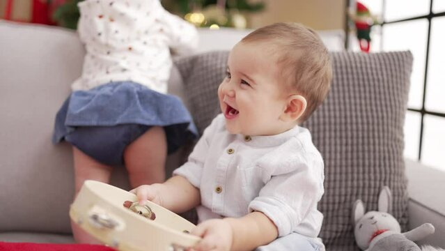 Adorable toddler holding tambourine sitting on sofa by christmas tree at home