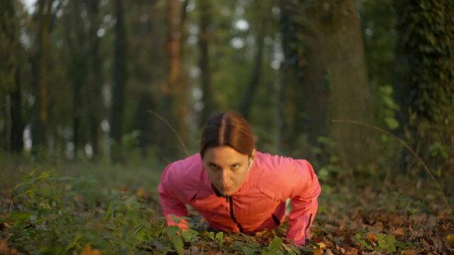 Fitness young female doing push ups exercise in the forest at sunset. Healthy young female working out in slow-motion