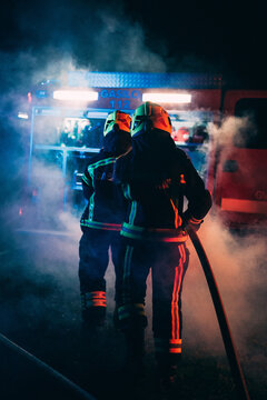 Firefighters with a hose walking towards firetruck.