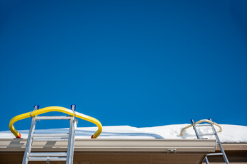 Ladder and safety hook on a residential roof covered in snow as gutters are being installed. 