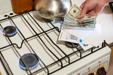Payment of utility services. Dollar bills, utility bills are held in their hands near a burning gas burner. The concept of increasing the cost of natural gas supply and payment.